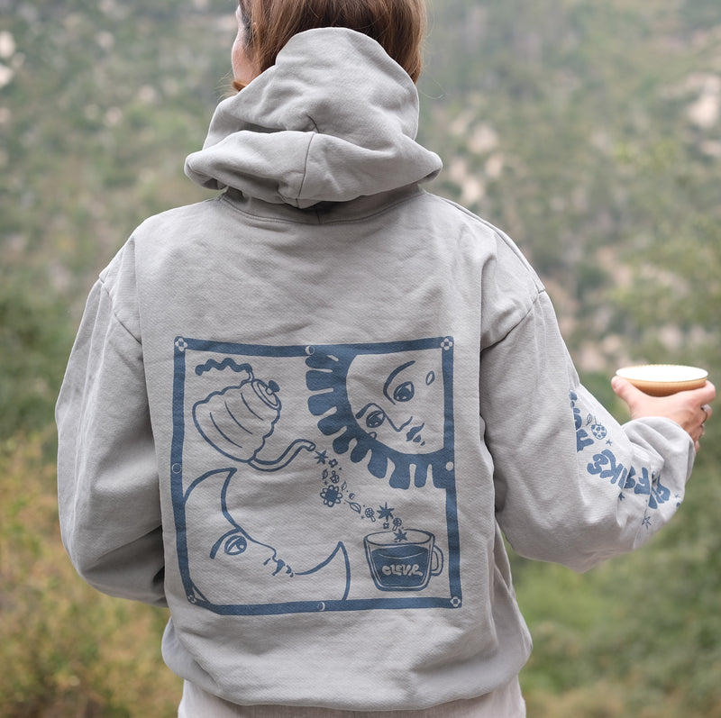 Person wearing hoodie and showing back image of sun, moon, and Clevr being poured into a cup